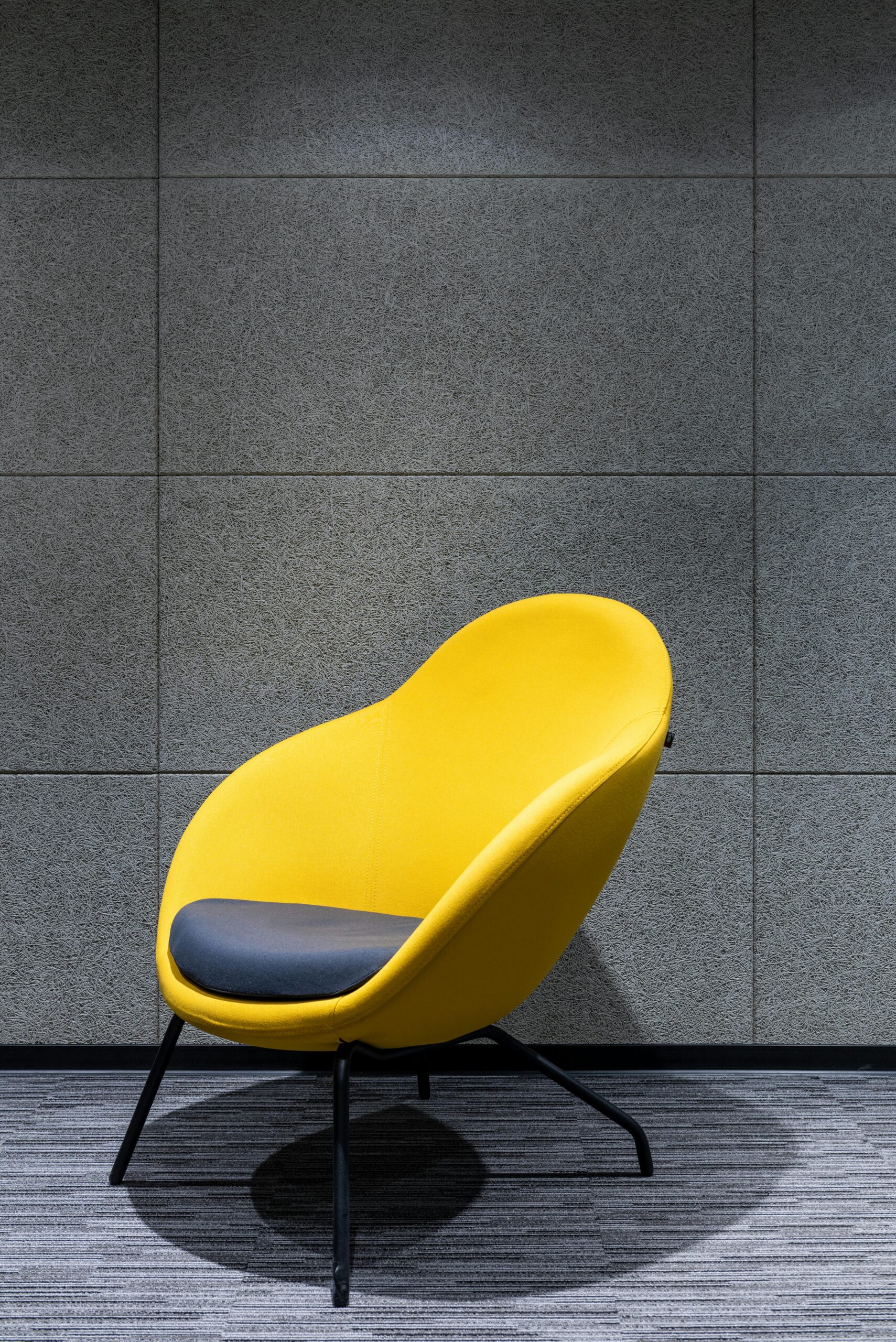 Gray pillow on comfortable chair with yellow textile and armrests placed on floor near gray wall in modern light studio